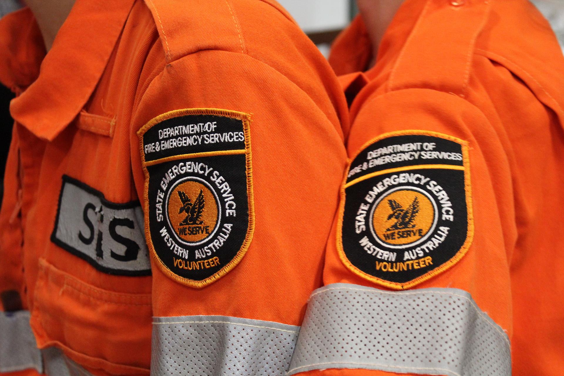 left shoulder of two individuals in orange overalls, the overalls have the state emergency services logo sewed on them